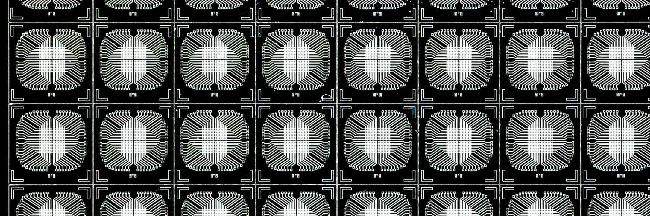 A repeating grid of memristor crossbar dies on a wafer, each cell showing a symmetric fan of fine electrode traces around a central crosspoint.